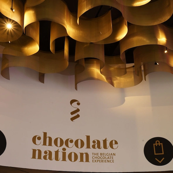 Design Metal Mesh Chocolate Nation Antwerp-Design metaalgaas van messing, vervaardigd voor de architect van het museum Chocolate Nation, met een uniek patroon dat grote chocoladekrullen imiteert. Deze artistieke en speelse bekleding combineert luxe en vakmanschap, en vormt een opvallend architecturaal accent binnen het museuminterieur.